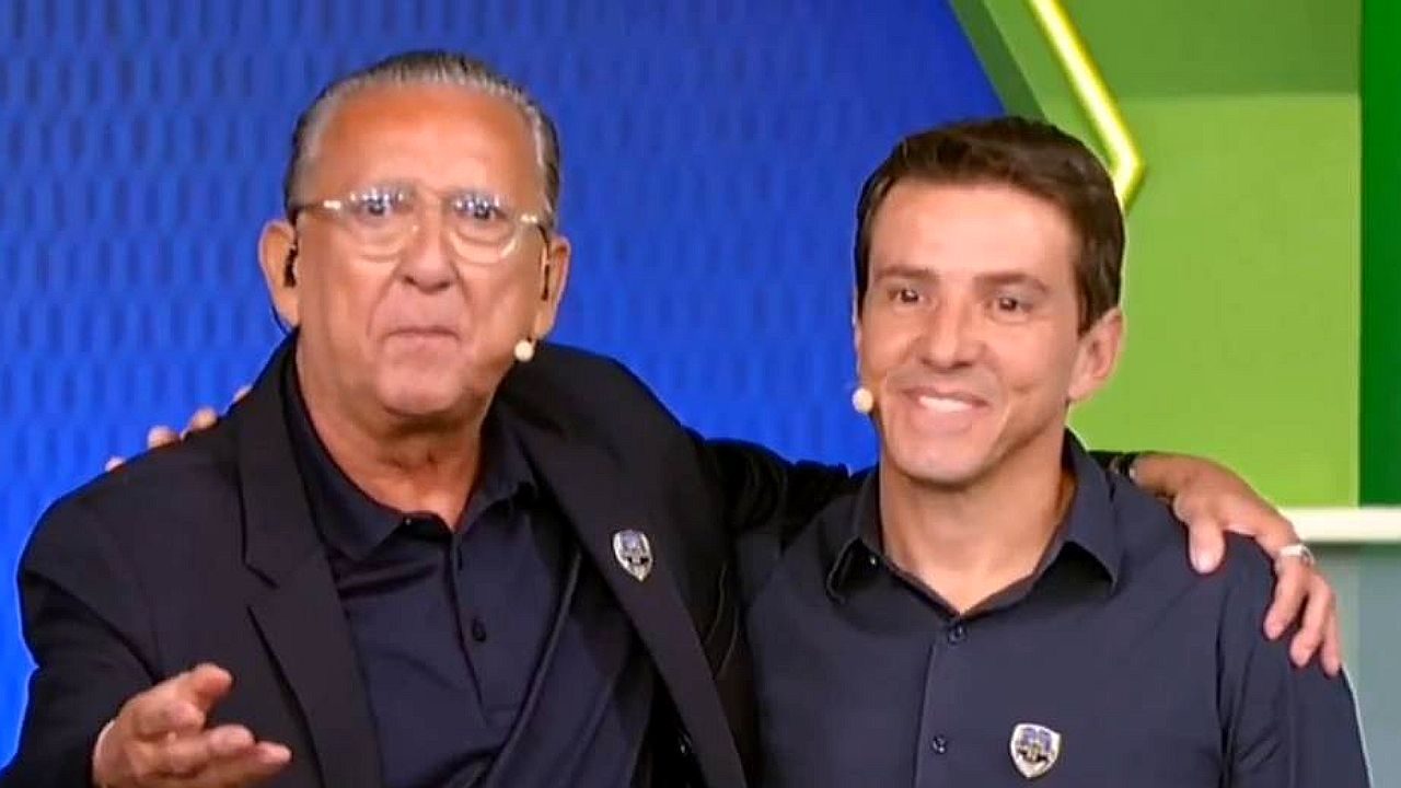 Dois apresentadores de TV lado a lado no estúdio com microfones de lapela durante programa ao vivo