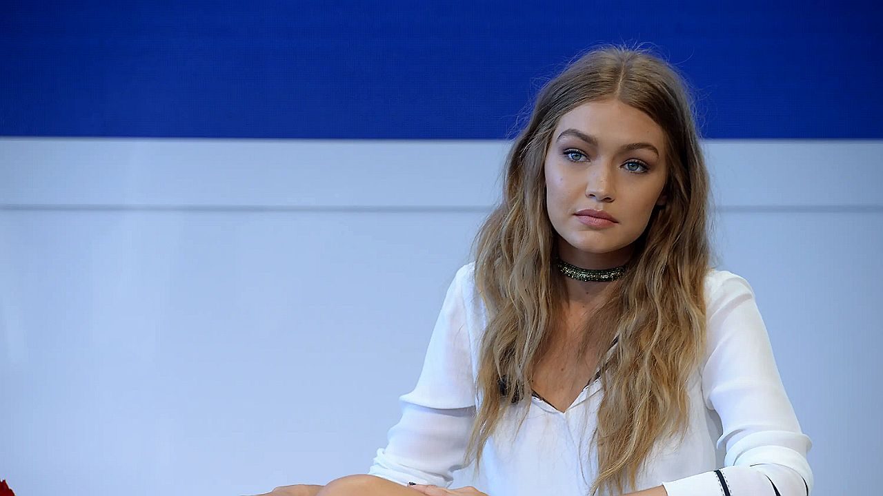 Mulher de blusa branca e gargantilha preta observa com expressão séria em ambiente corporativo