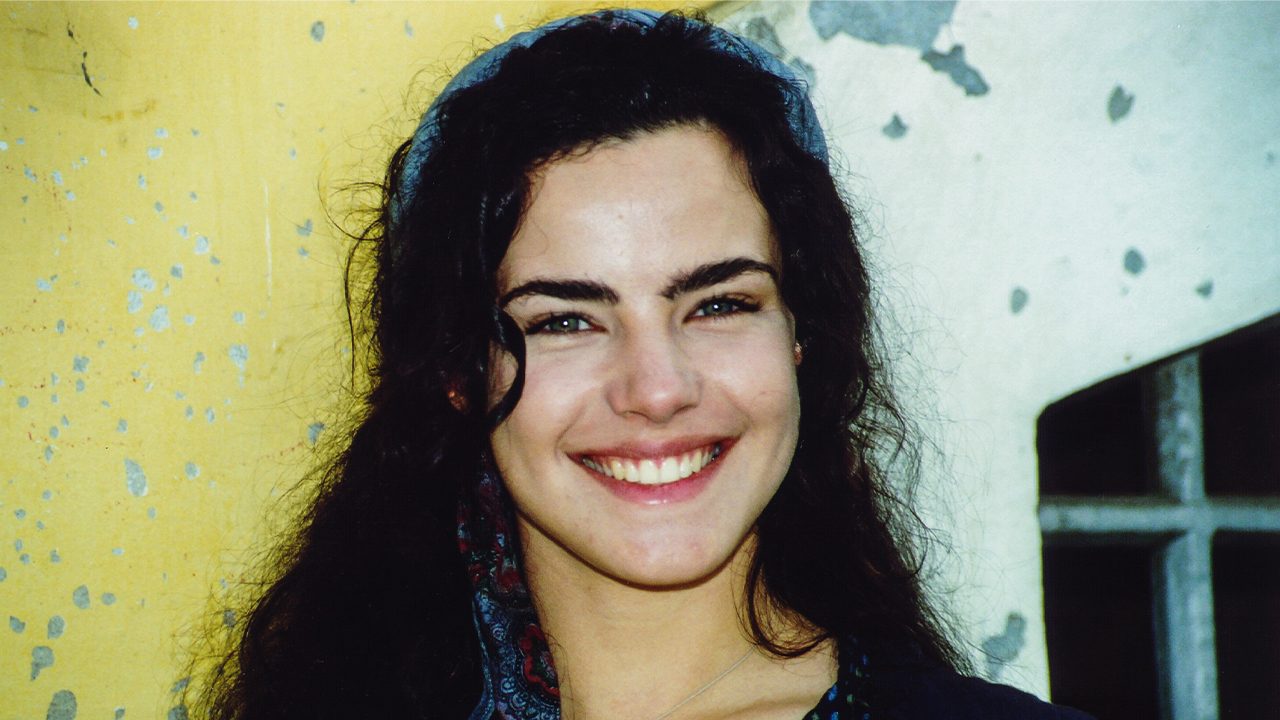 Ana Paula Arósio sorrindo caracterizada como Giuliana com lenço azul no cabelo em cena da novela Terra Nostra