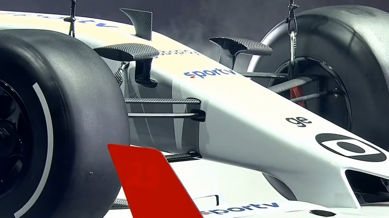 Detalhe do bico e das asas dianteiras de um carro de Fórmula 1 branco, exibindo componentes de fibra de carbono, pneus slick largos e logotipos de patrocinadores