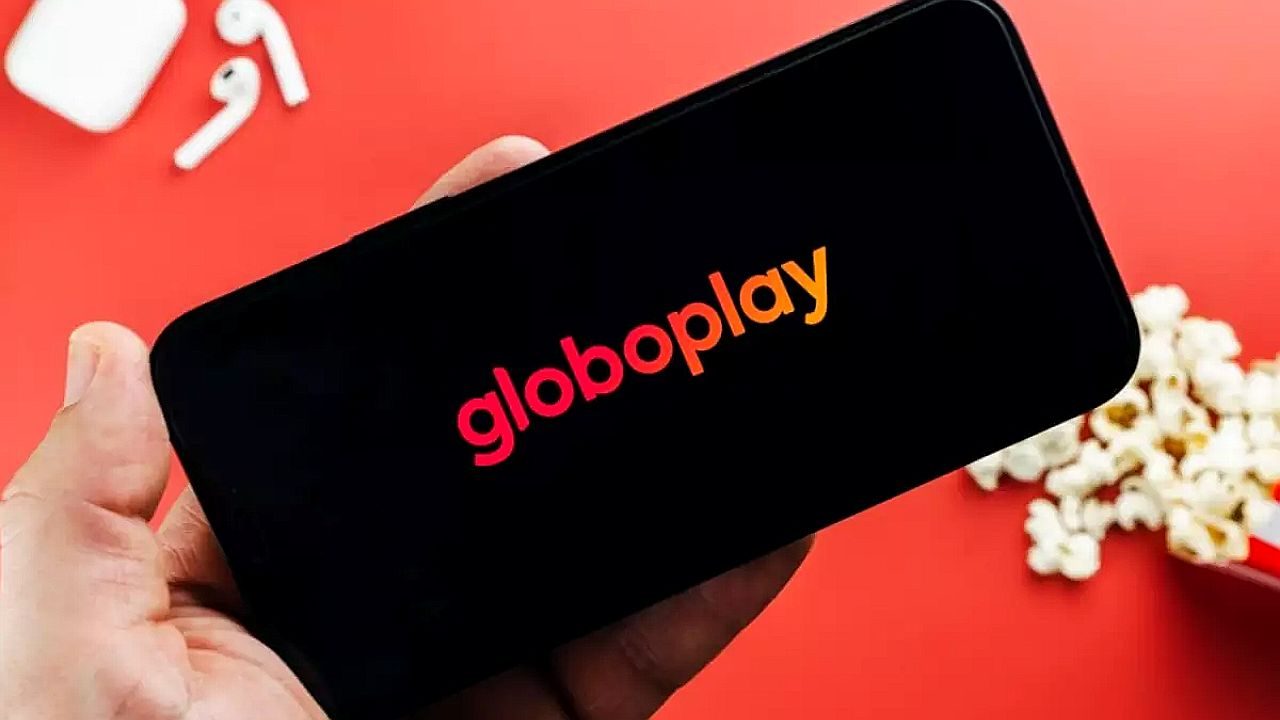 Celular exibe logotipo do Globoplay em tela preta sobre fundo vermelho com pipoca e fones de ouvido ao redor
