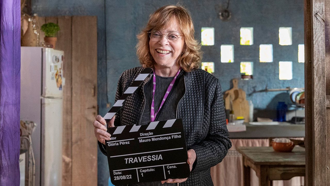Gloria Perez sorrindo e segurando claquete da novela Travessia em set de gravação da Globo