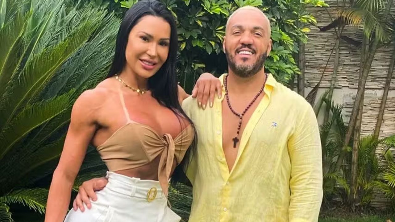 Gracyanne Barbosa com top bege e o cantor Belo de camisa amarela, ambos sorrindo em um jardim