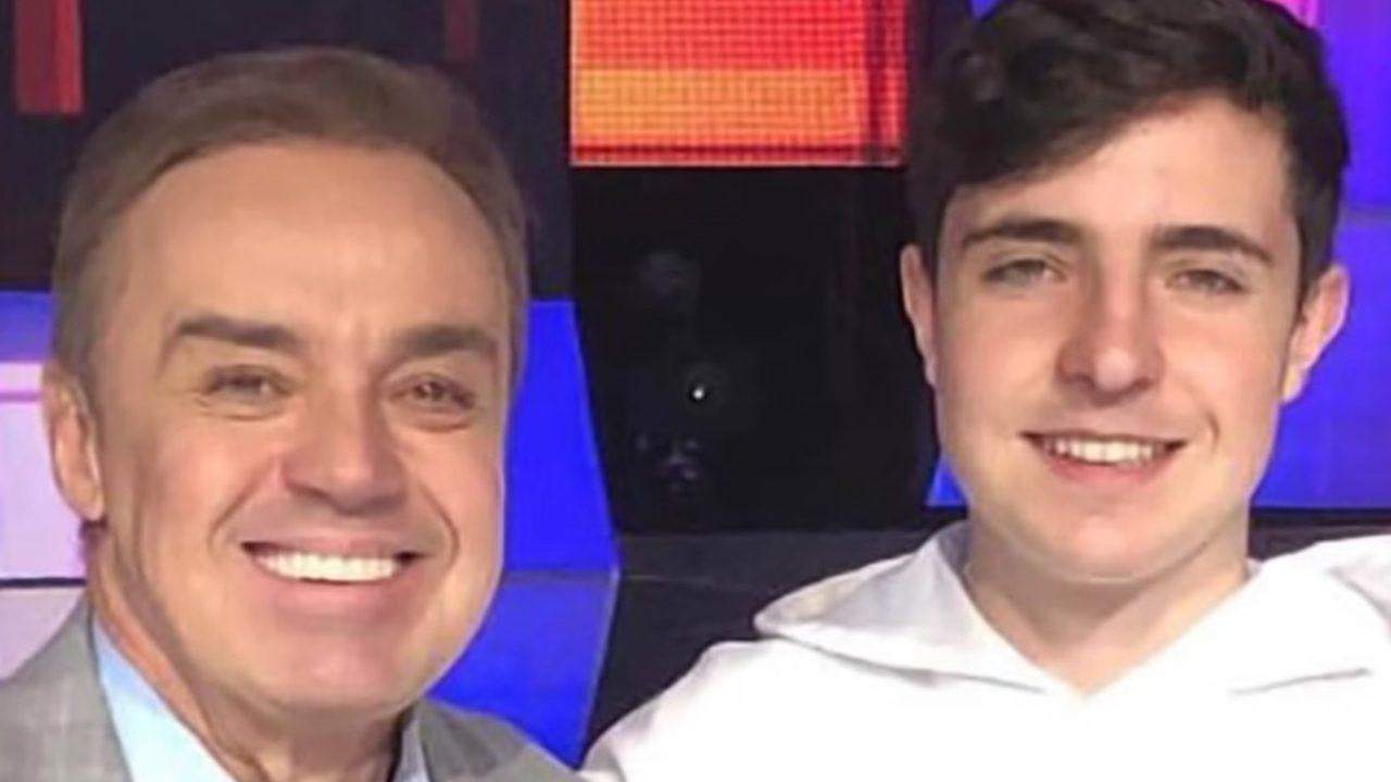 Gugu Liberato e João Augusto Liberato sorrindo juntos em estúdio com painel colorido ao fundo