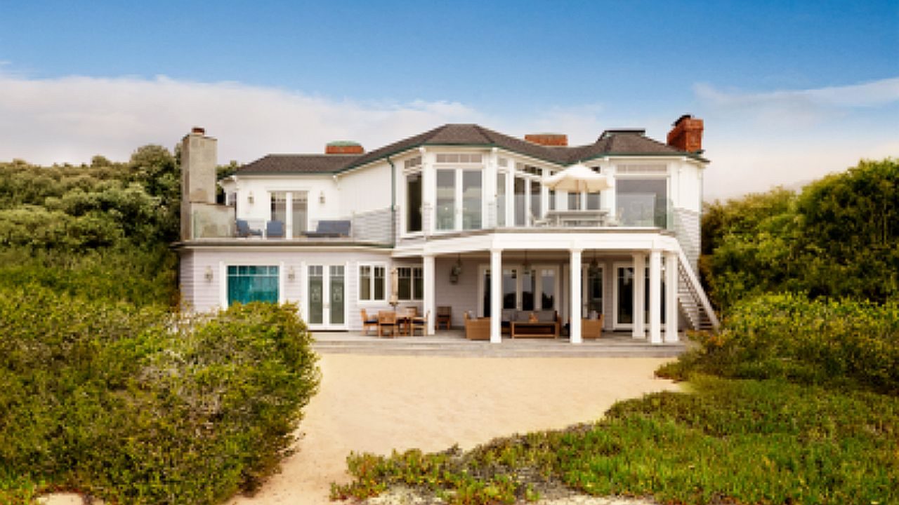 Casa de luxo com dois andares e varanda ampla cercada por vegetação em área litorânea com vista para a praia