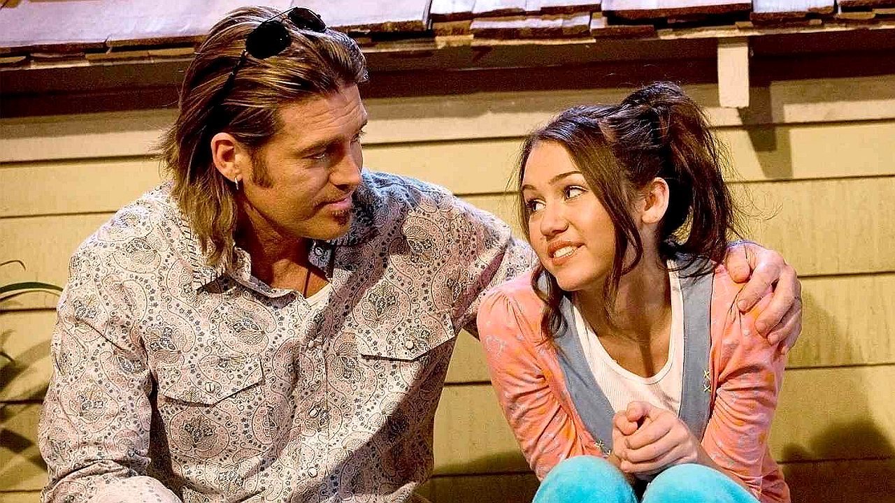 Texto Alternativo disse: Homem abraça jovem enquanto conversam sentados em escada em cena de filme com clima familiar