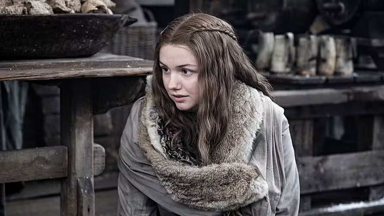 Atriz agachada em cenário medieval durante cena da série Game of Thrones