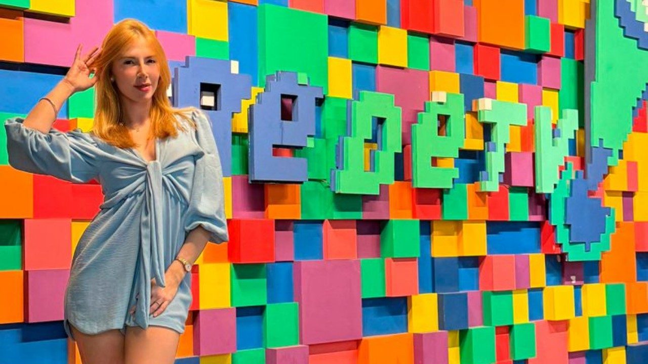 Heloisa Herold posa diante de painel colorido com cubos e logotipo da RedeTV! em ambiente interno da emissora