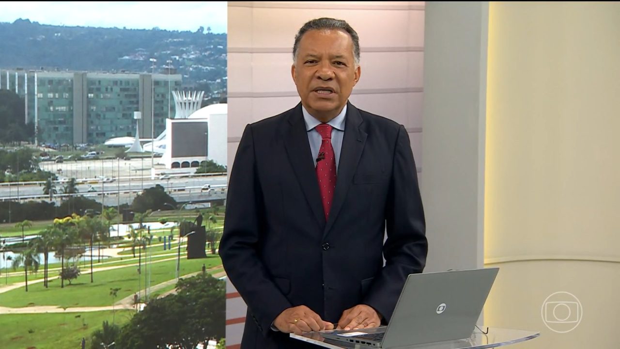 Heraldo Pereira apresenta jornal da TV Globo diante de telão com imagem de Brasília e laptop no estúdio.