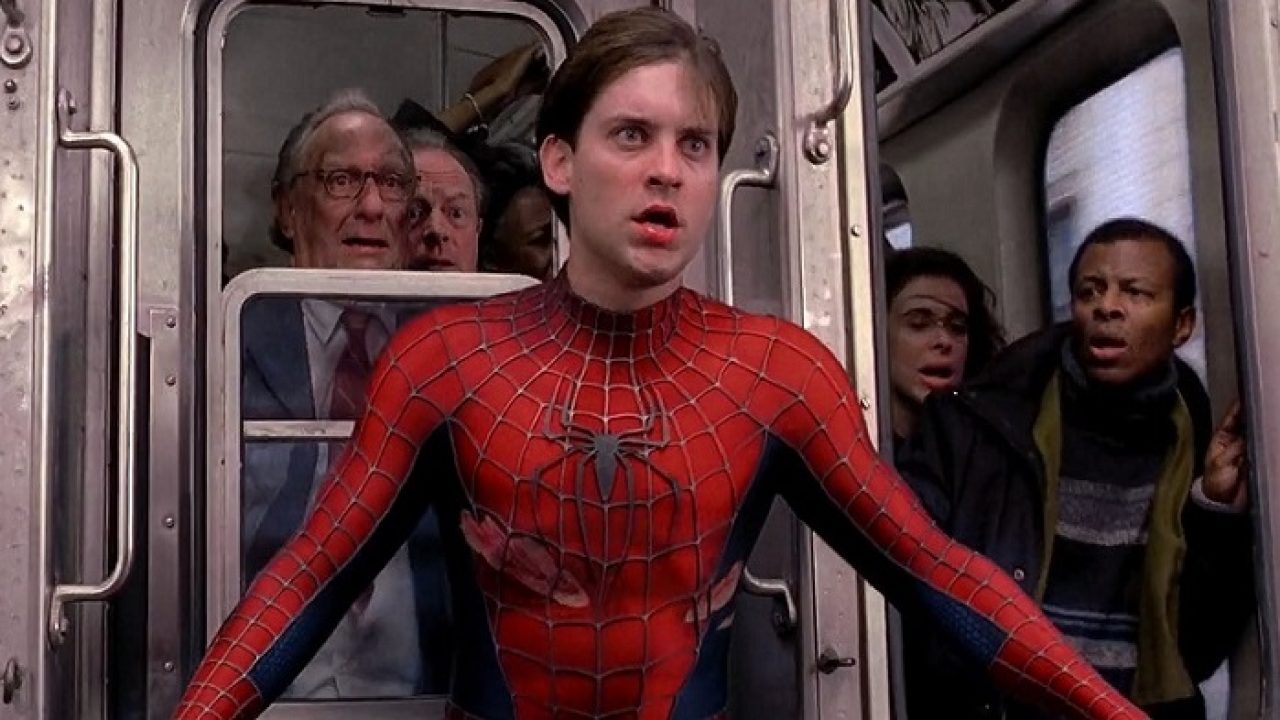 Foto de um homem vestido com a roupa do Homem Aranha e um trem atrás com inúmeras pessoas