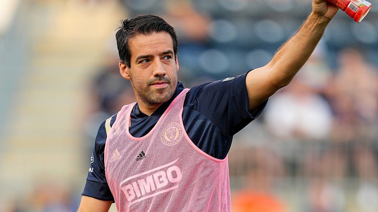 Jogador de futebol em aquecimento levanta garrafa durante treino em campo com uniforme de treino patrocinado