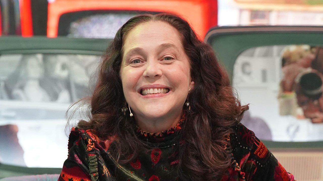 Atriz Isabela Garcia sorrindo com cabelo longo castanho e solto, usando blusa de veludo estampada em tom escuro