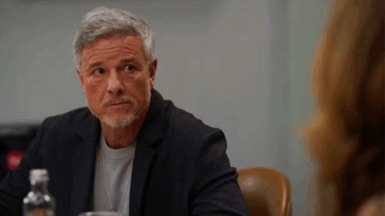Jaques sentado à mesa com expressão séria durante conversa em cena da novela Dona de Mim