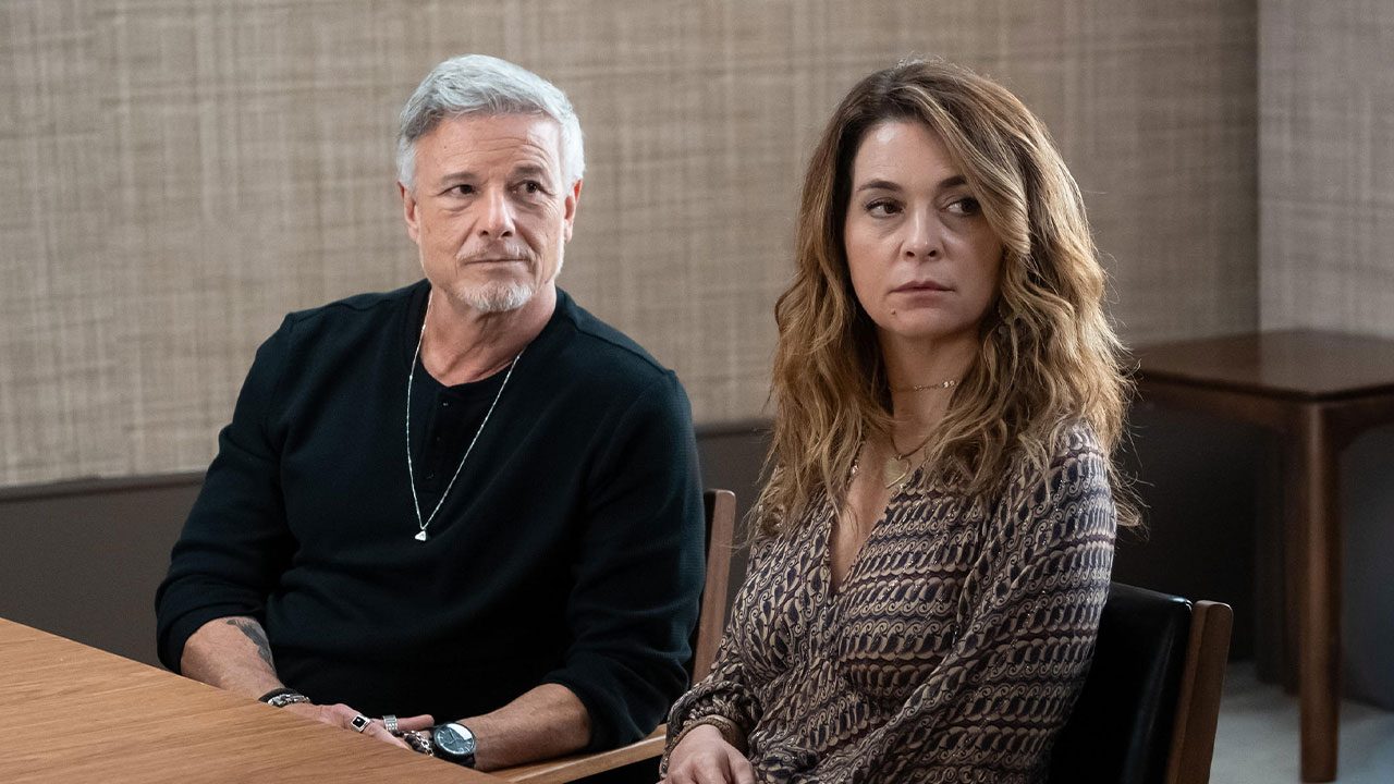 Jaques (Marcello Novaes), de camisa preta, e Filipa (Claudia Abreu), de blusa estampada, sentados à mesa com expressões sérias, em cena da novela Dona de Mim