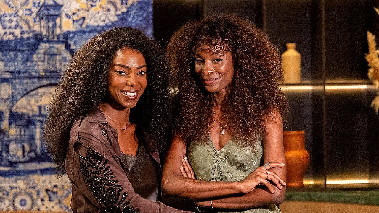 Jeniffer Dias e colega de elenco sorriem durante cena ambientada em casa em novela vertical