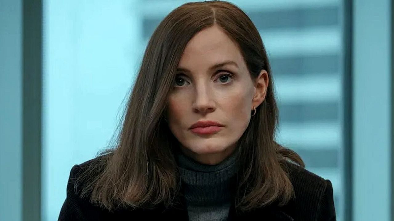 Mulher de cabelo castanho e expressão séria encara a câmera em ambiente corporativo