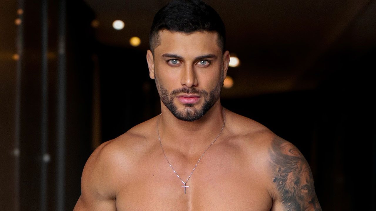 Jesus Luz de barba em close-up, olhando intensamente com olhos azuis, usando colar de cruz e sem camisa