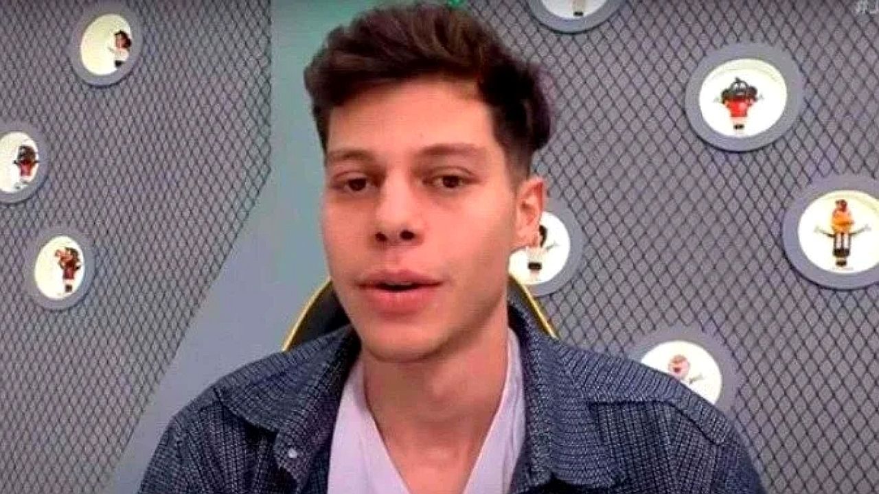 João Pedro fala durante transmissão online diante de parede decorada com quadros e iluminação circular
