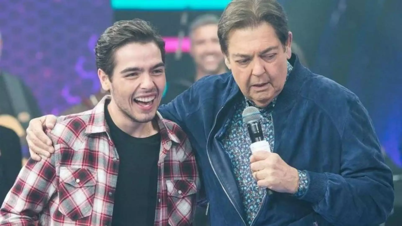 João Silva e Faustão juntos no palco do programa Domingão com microfone na mão e cenário iluminado