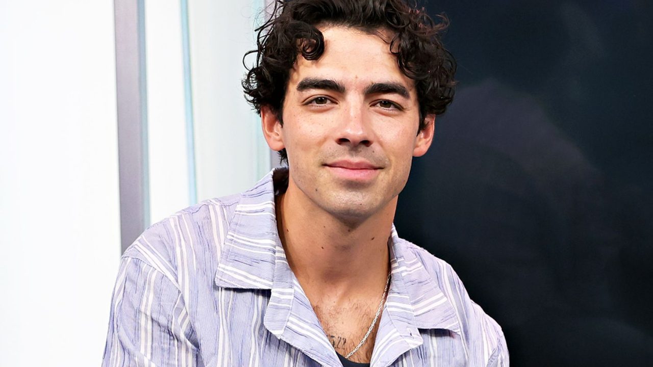 Joe Jonas em um terno claro com um fundo escuro