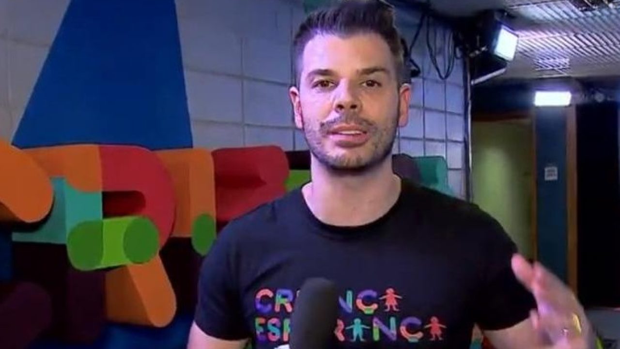 Ex-apresentador da Globo, Jonas Almeida de camisa preta atrás de um fundo colorido