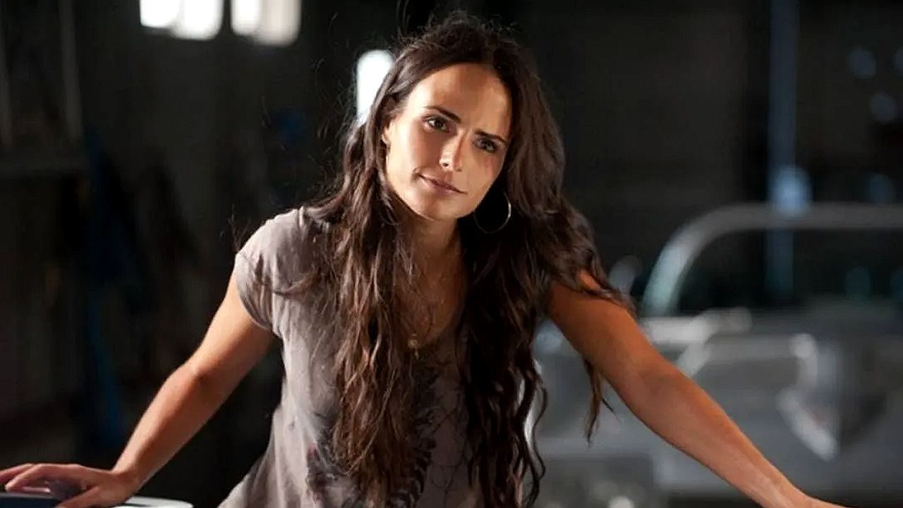 Mulher de cabelo longo apoia as mãos na mesa com expressão séria em cena dramática em ambiente interno