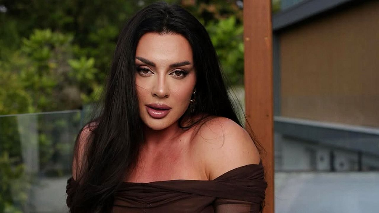 Mulher de cabelo longo posa com olhar direto para câmera em ambiente externo com vegetação ao fundo