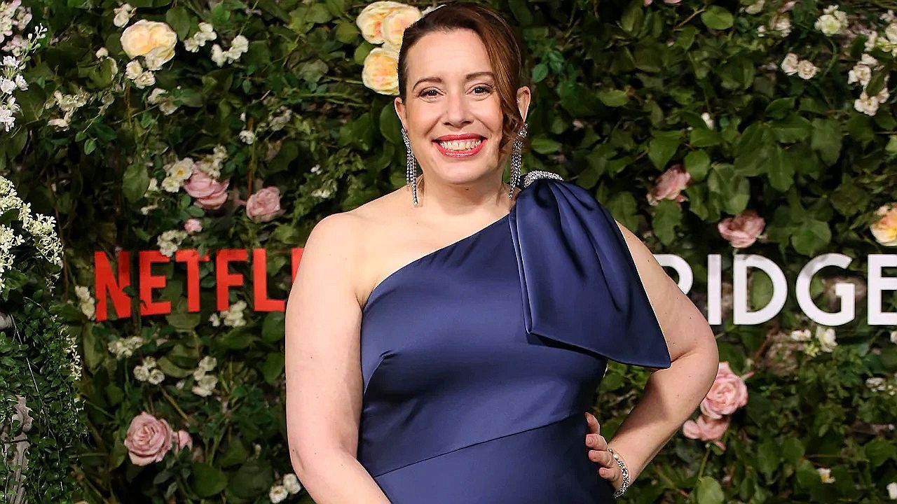 Artista posa sorrindo em evento da Netflix com vestido azul em frente a painel floral com logotipo Bridgerton