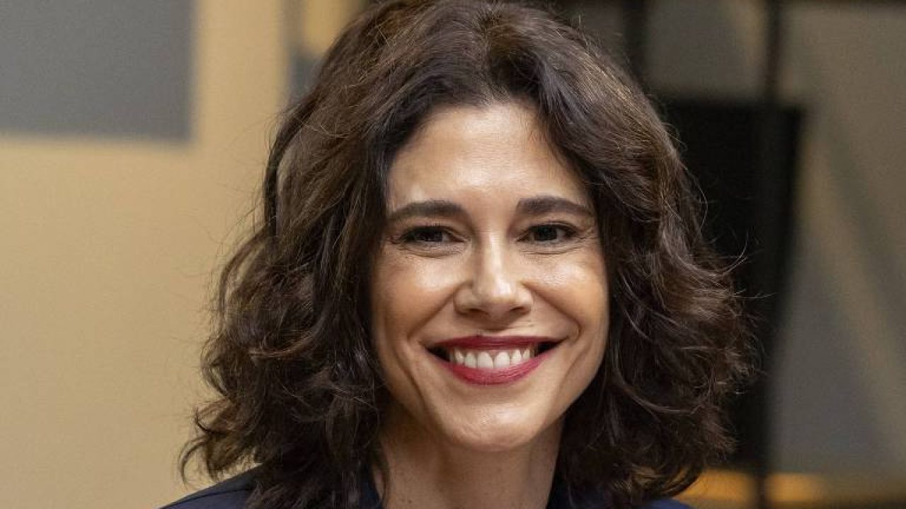 Juliana Martins sorrindo em ambiente interno com iluminação suave ao fundo