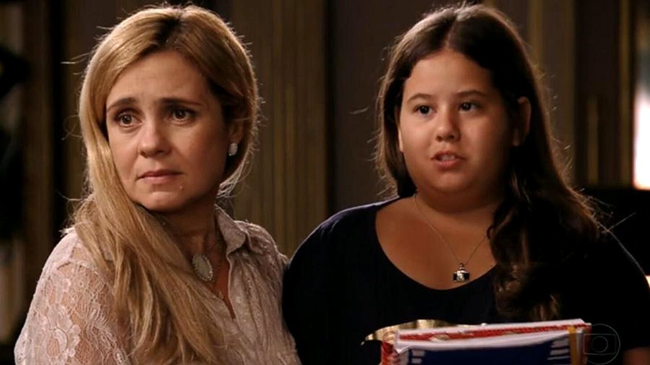 Mulher e menina com expressão preocupada seguram caderno em cena de novela da TV Globo