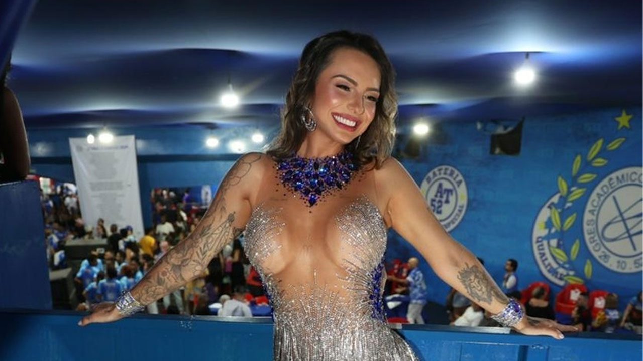 Karol Rosalin sorri com fantasia de carnaval transparente e brilhante, com pedrarias azuis, em uma quadra de escola de samba