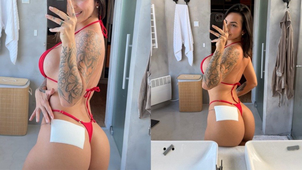 Karol Rosalin faz selfie de biquíni vermelho diante do espelho em banheiro com curativo no quadril e tatuagens no braço