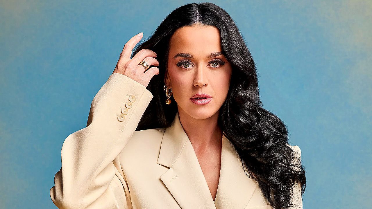 Mulher de blazer bege posa com cabelo solto em ensaio fotográfico com fundo azul