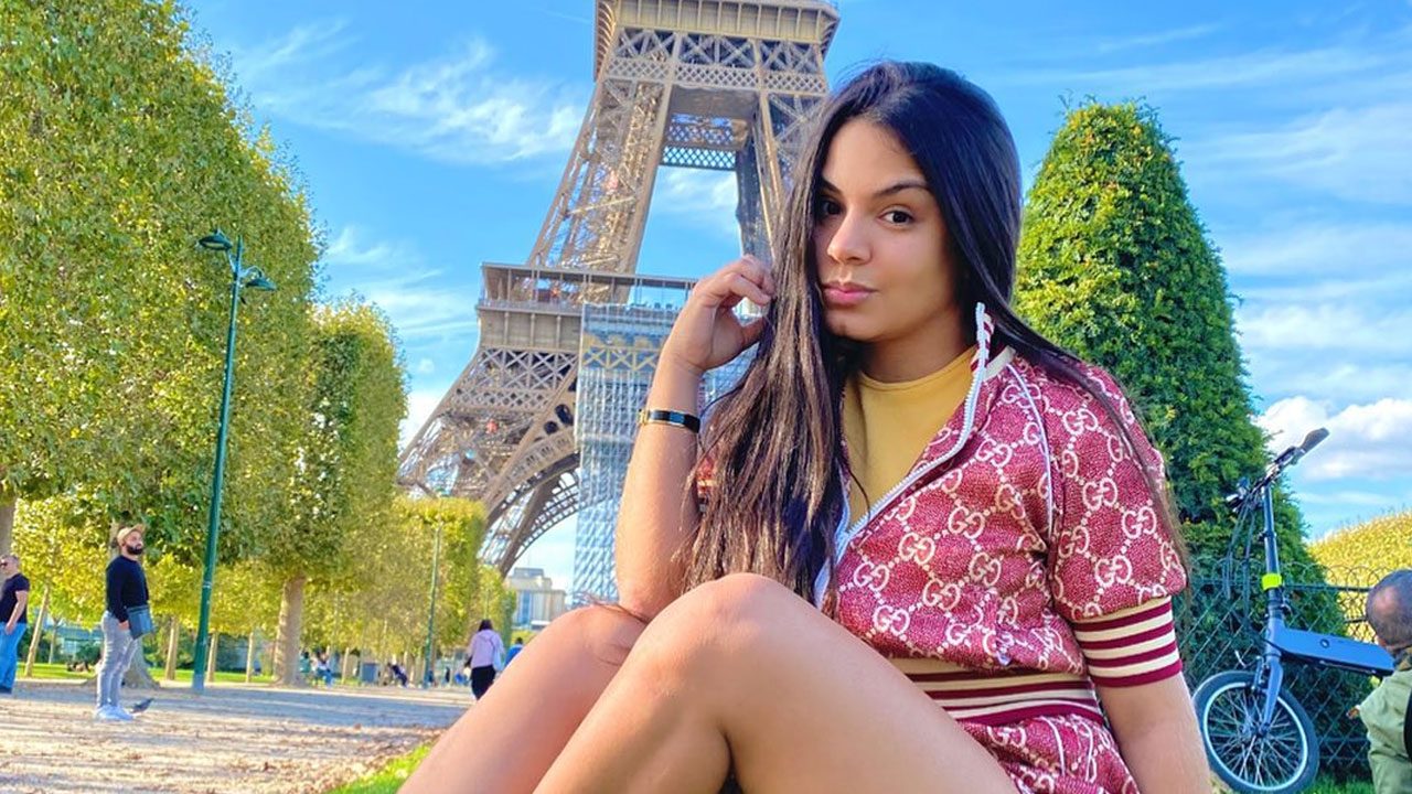 Kéllyta Tharsys sentada em frente à Torre Eiffel em Paris usando conjunto vermelho estampado