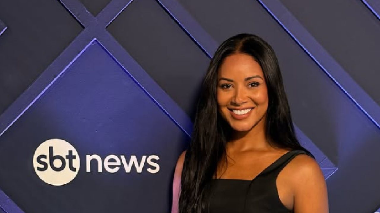 Mulher sorrindo de vestido preto em frente ao painel azul do SBT News iluminado por luz lateral