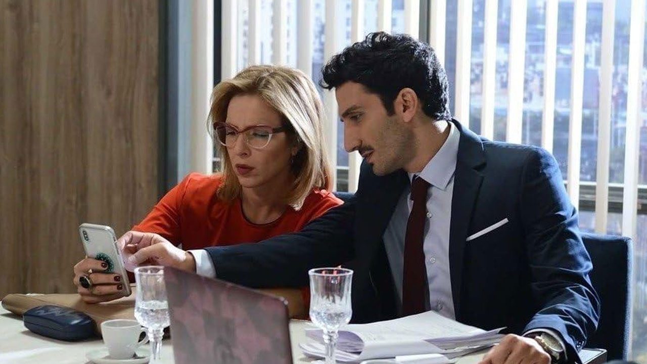 Laura (Carla Peterson) mostra celular para Gastão (Juan Minujín) em cena de escritório na novela 100 días para Enamorarse