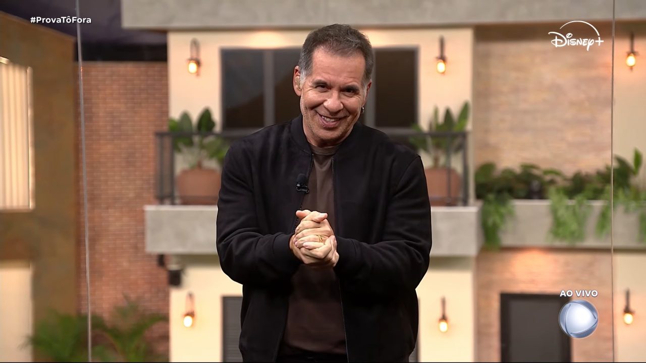 Leandro Hassum sorri e junta as mãos durante a Casa do Patrão, ao vivo, com cenário de casa ao fundo em transmissão feita pela Record.