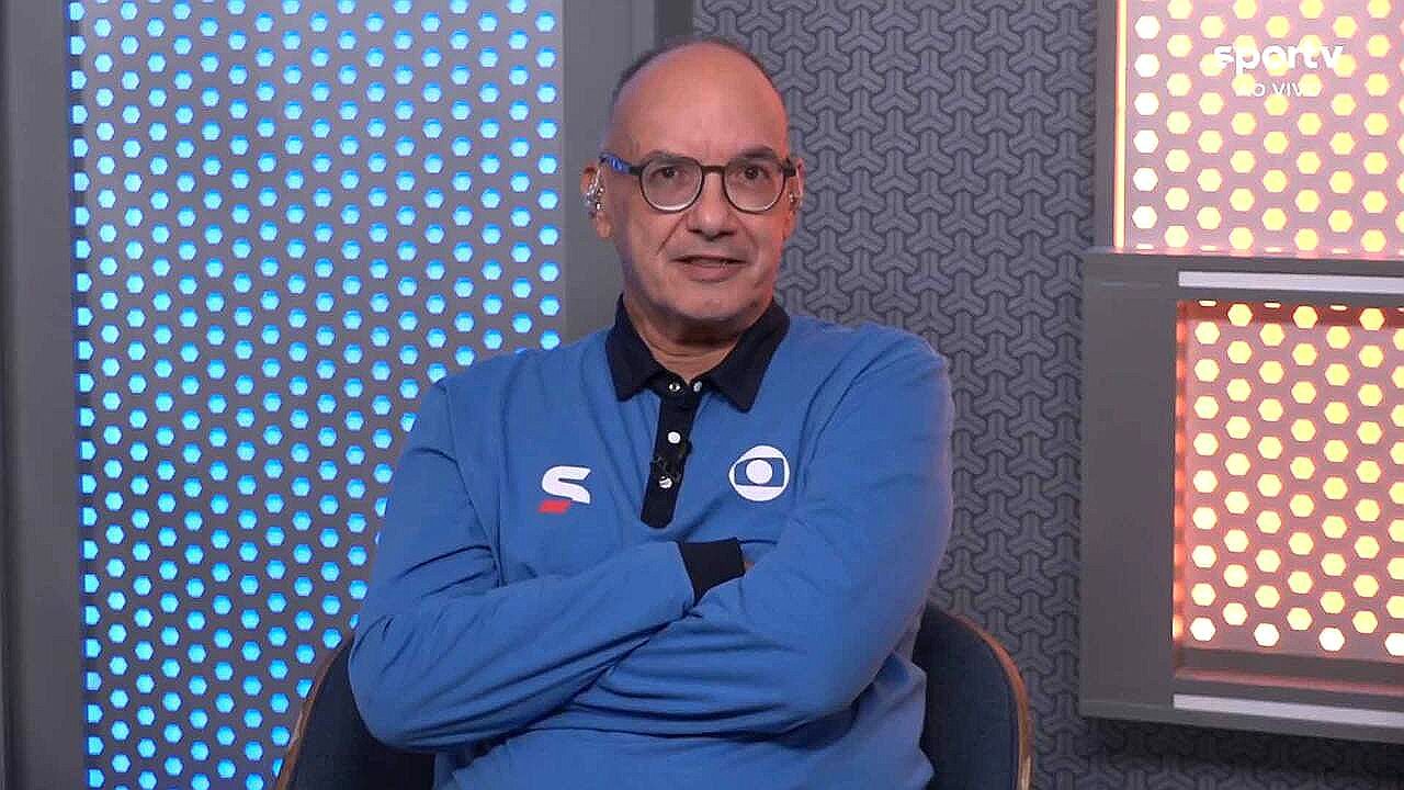 Comentarista usa camisa do sportv com braços cruzados durante programa ao vivo em estúdio iluminado