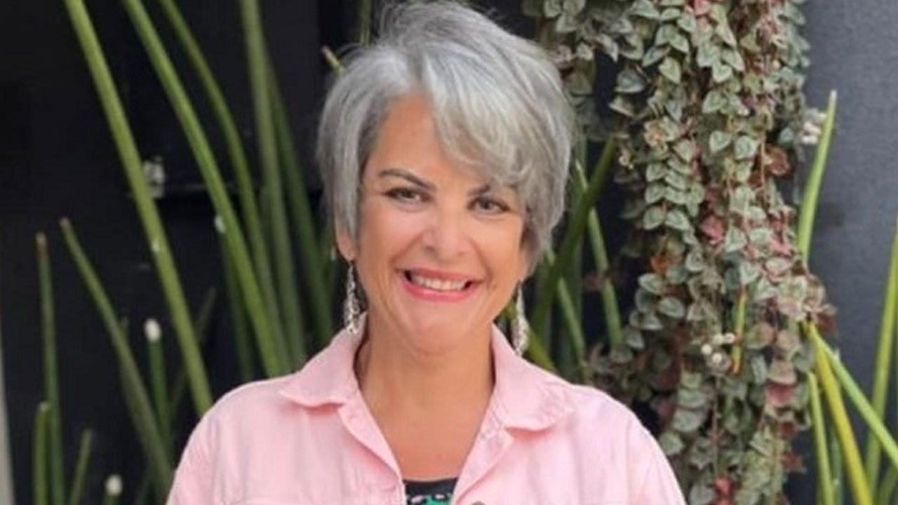 Leonor Corrêa sorrindo com camisa rosa clara em foto ao ar livre com plantas ao fundo