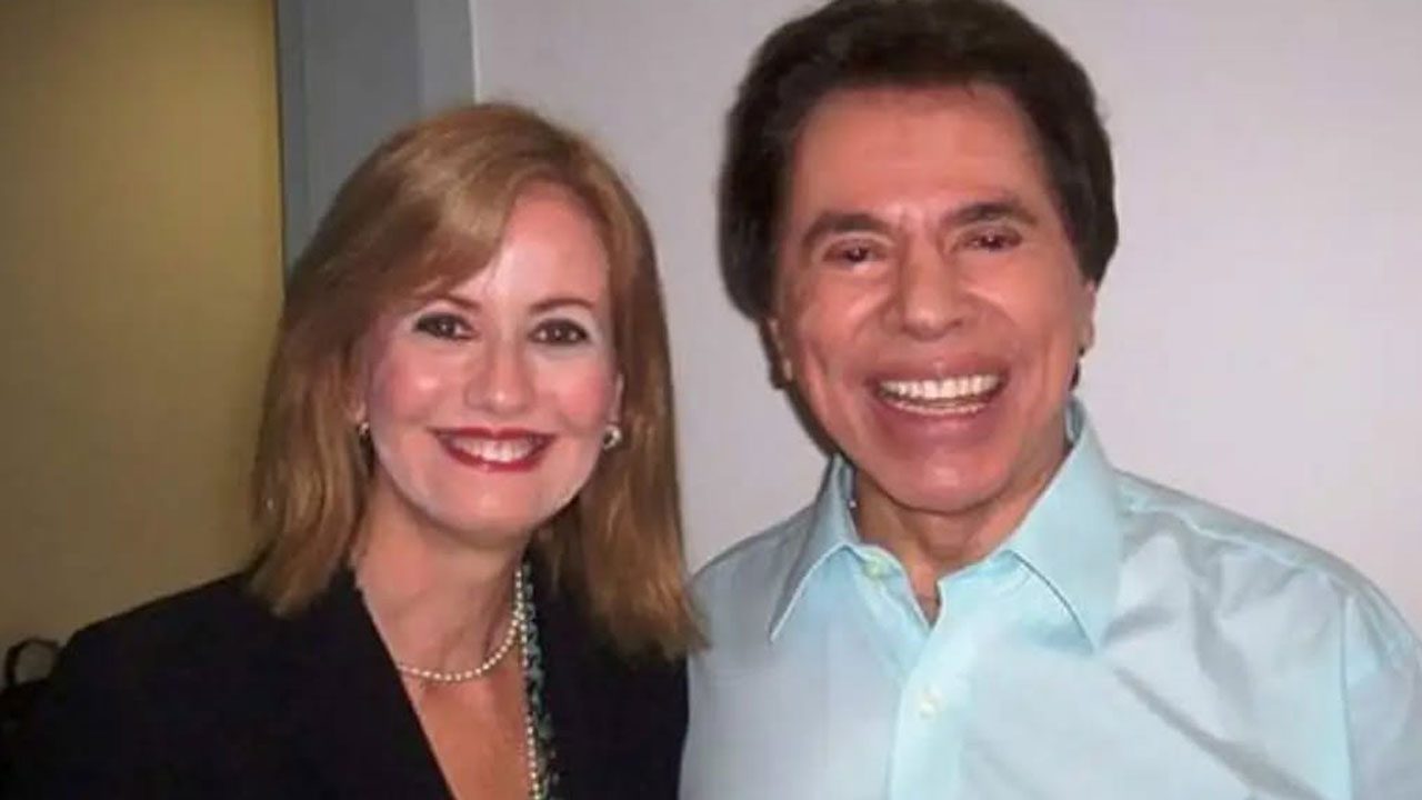 Letícia Dornelles e Silvio Santos sorrindo juntos em foto posada com fundo neutro
