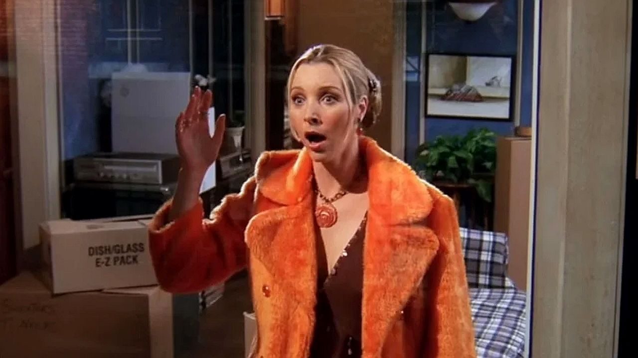 Phoebe levanta a mão suja e reage surpresa em cena da série Friends dentro do apartamento