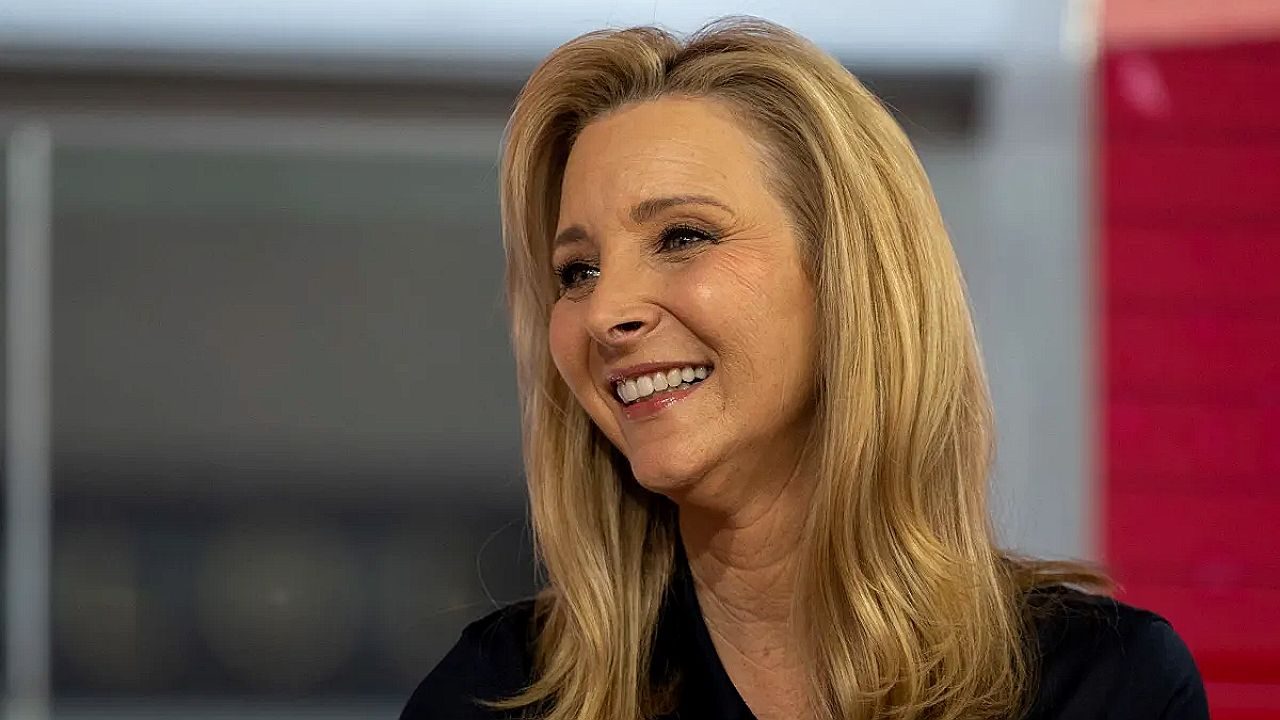 Mulher loira sorri durante entrevista em estúdio de televisão
