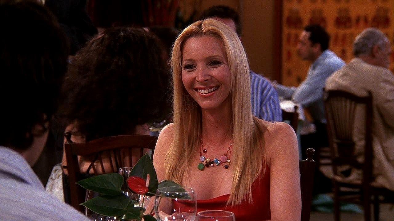 Phoebe sorri durante encontro em restaurante em cena da série Friends