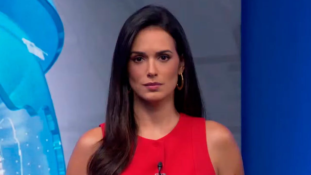 Lívia Nepomuceno com expressão séria, vestindo roupa vermelha, durante apresentação do Jornal da Band