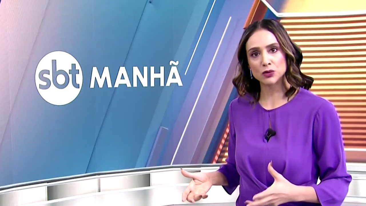 Lívia Zanolini no estúdio do SBT Manhã usando vestido roxo ao lado do logotipo do telejornal