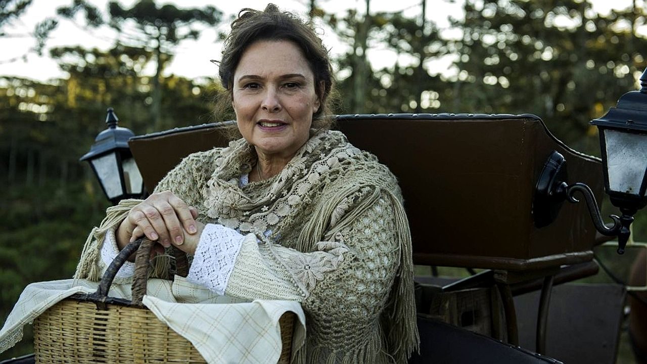 Louise Cardoso segura cesta em carruagem durante cena ambientada no campo