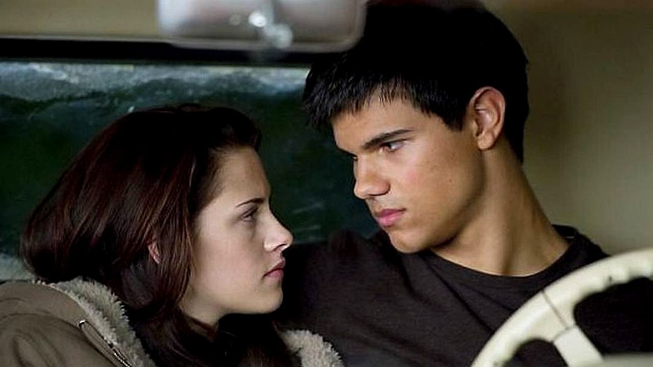 Jovem casal troca olhares intensos enquanto está sentado dentro de um carro em cena romântica de filme