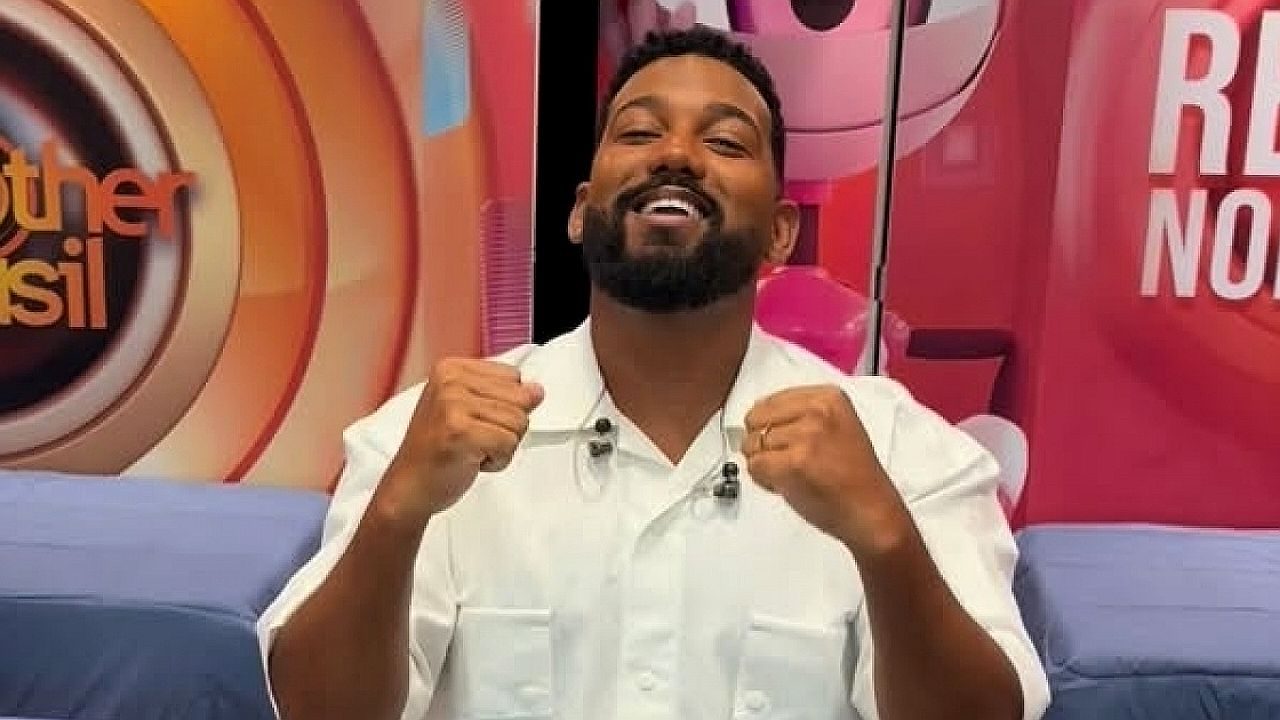 Homem de barba sorri e levanta os punhos durante programa de entretenimento em estúdio da Globo