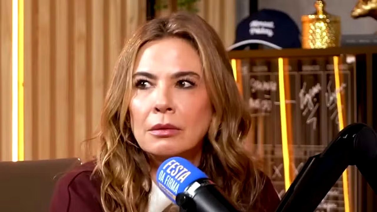 Luciana Gimenez durante entrevista em podcast com microfone do Festa da Firma e troféus ao fundo