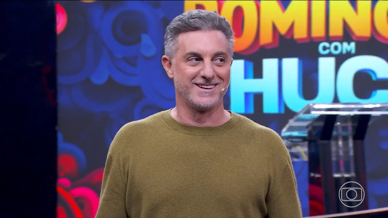 Imagem do apresentador Luciano Huck sorrindo no palco do Domingão com Huck, durante programa exibido ao vivo na TV Globo.
